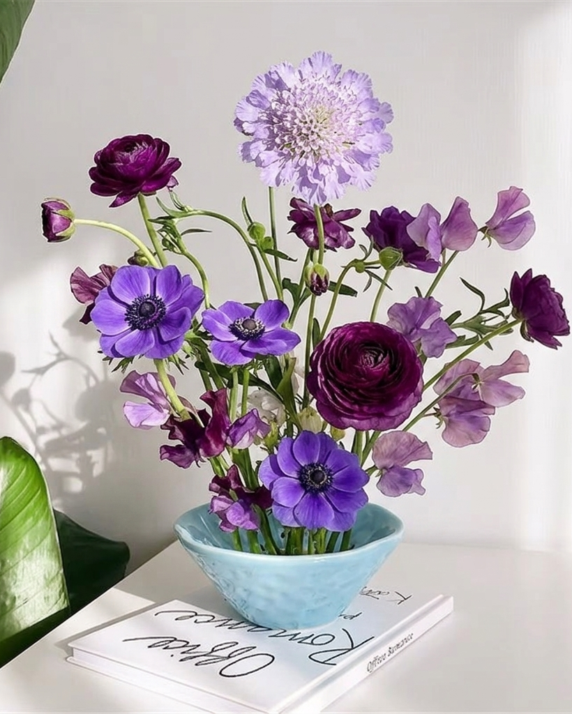 Bouquet of purple and pink flowers in a blue vase on a white surface with a white background