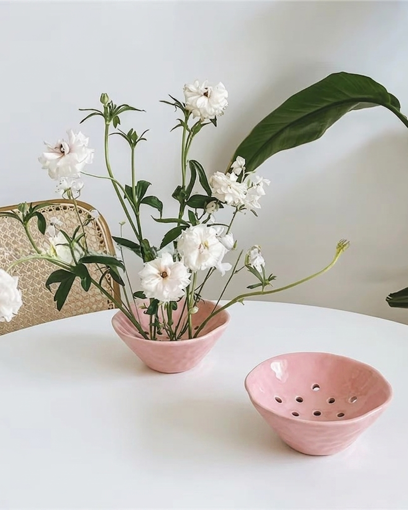 Pink ceramic vase with white flowers on a white surface