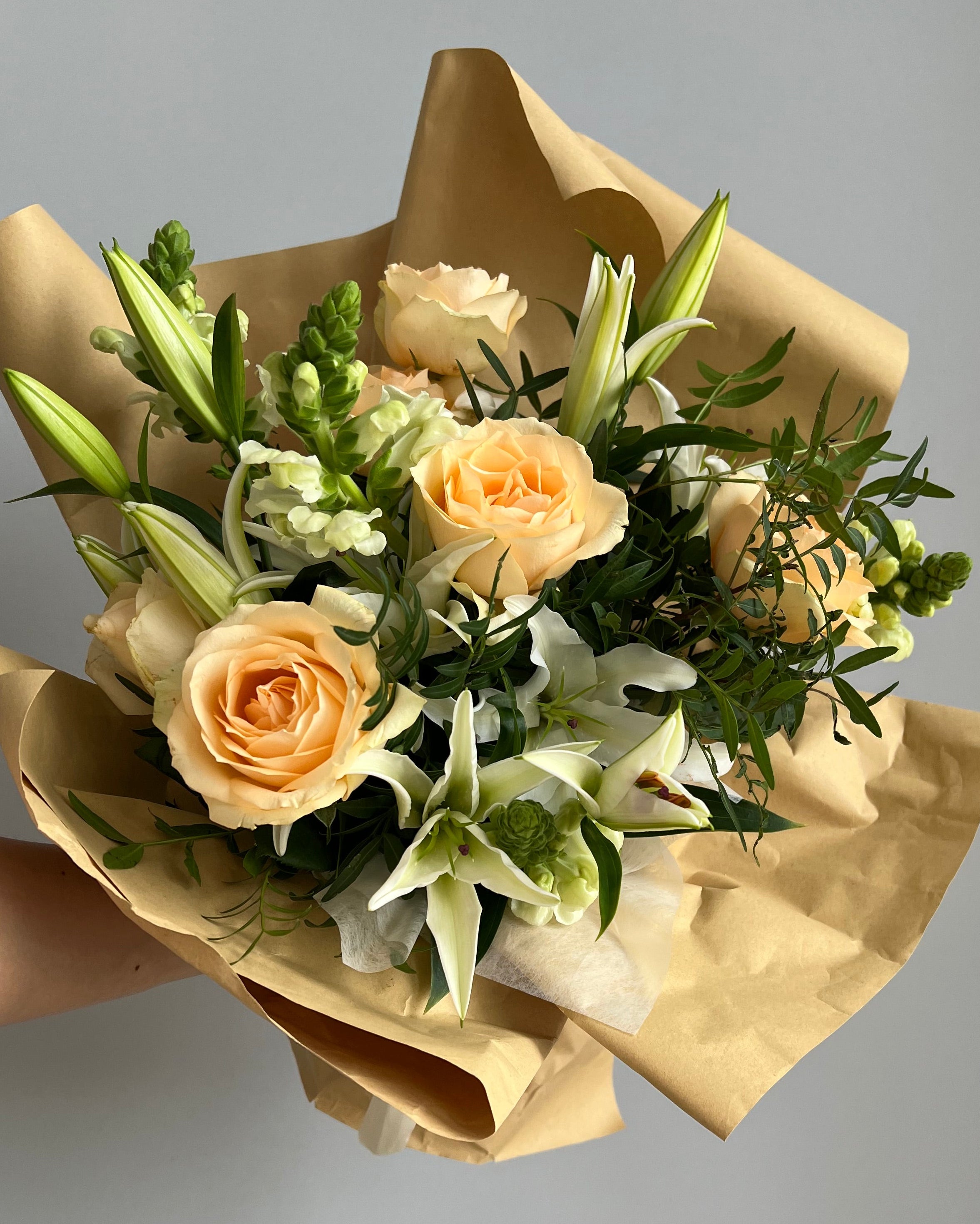 Bouquet of flowers wrapped in brown paper against a plain background
