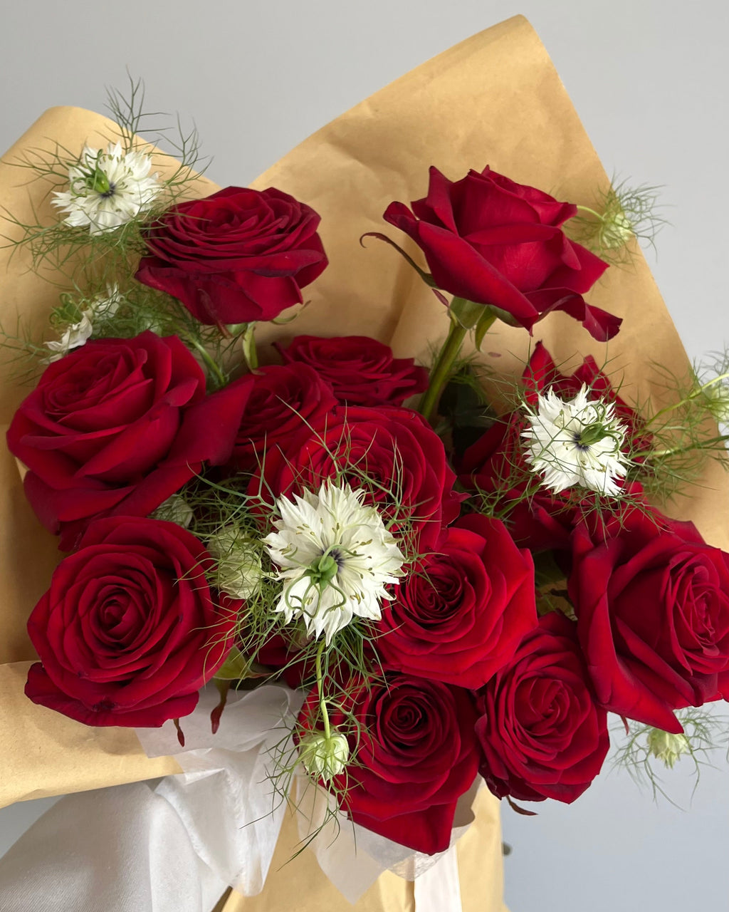 Bouquet of red roses with white flowers wrapped in gold paper on a light gray background