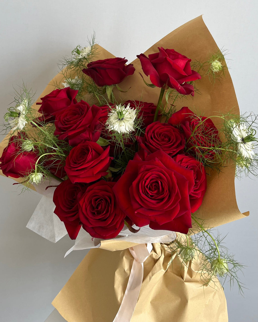 Bouquet of red roses wrapped in brown paper on a light gray background