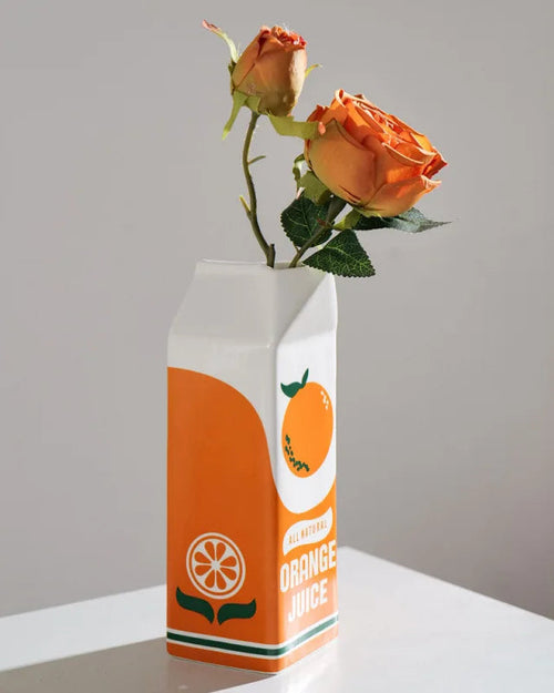 Orange juice carton repurposed as a vase with orange roses on a light background